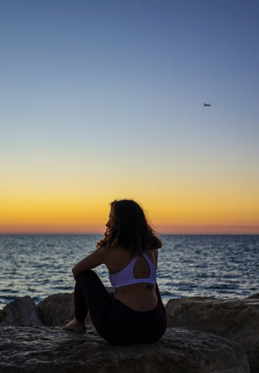 a woman is sitting on rocks overlooking the ocean