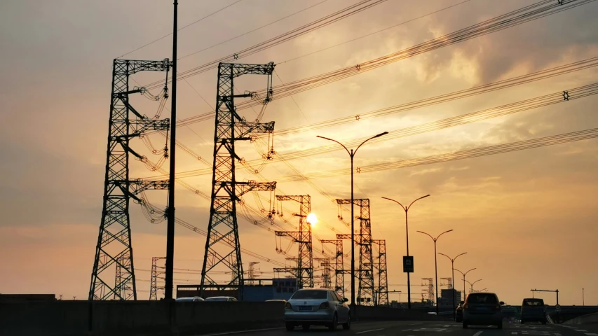 the sun setting behind two high - voltage power lines on an interstate highway