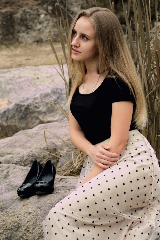 a woman in black shirt sitting on a rock with shoes