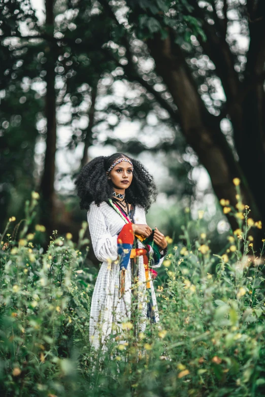 young black woman in a long dress and beaded headpiece holding a piece of fabric with her arms