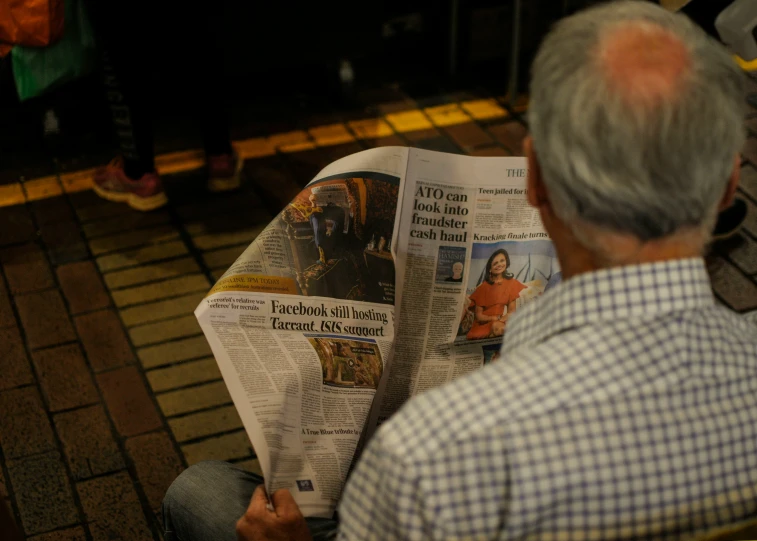 the man is reading the newspaper as he sits outside