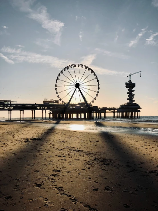 ferris wheel sitting on the edge of a sandy beach near a pier