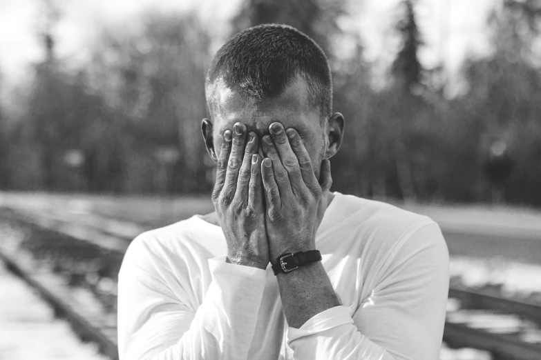 a man is covering his eyes as he stands in front of train tracks