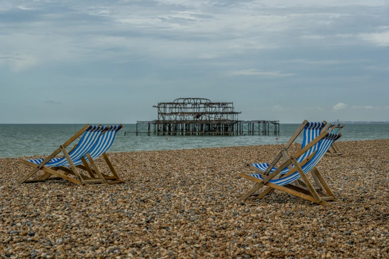 two lawn chairs facing the ocean with a wooden structure in the background