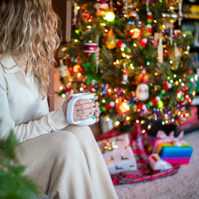 a woman sitting in front of a christmas tree drinking coffee