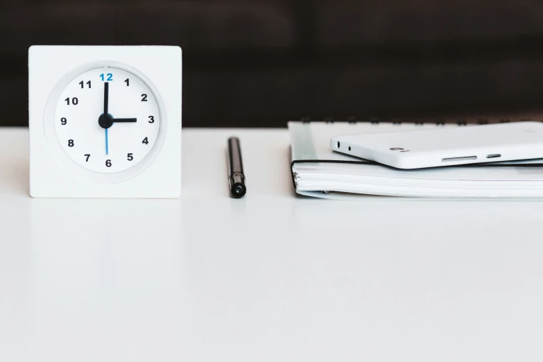 a white clock on a table near a pen