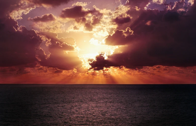 sun peeking through dark clouds in front of the ocean