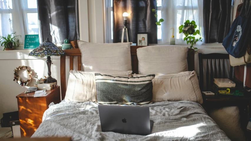 a bed sitting under some windows and a laptop computer