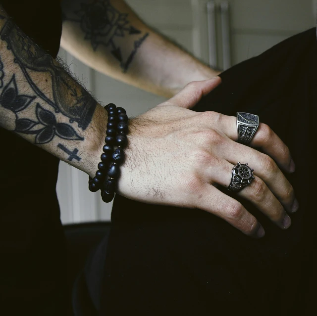 a tattooed arm wearing two different rings and black beads