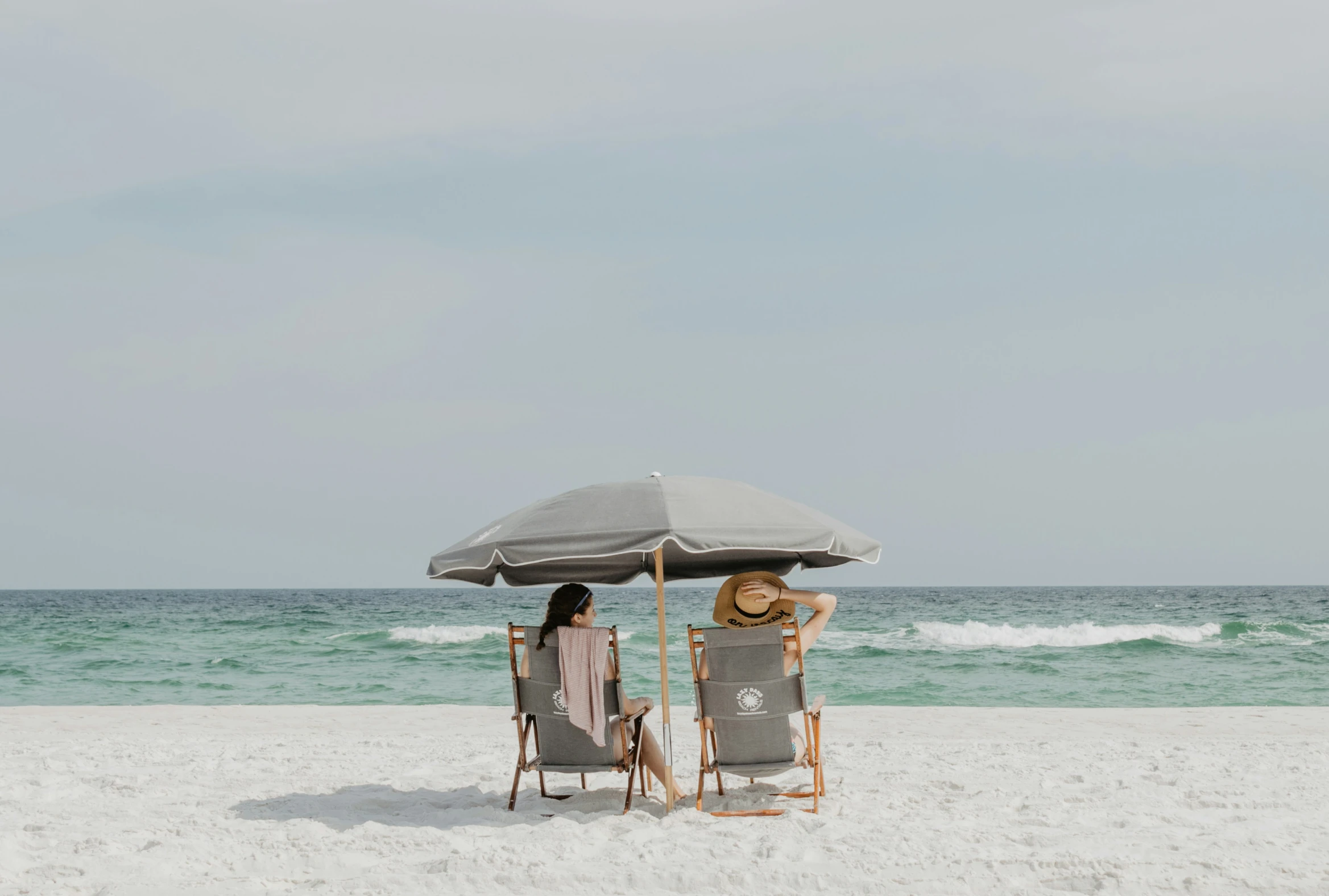 a couple of women sit under a large umbrella