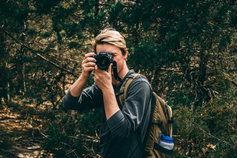 a man in grey jacket taking a po of trees and bushes