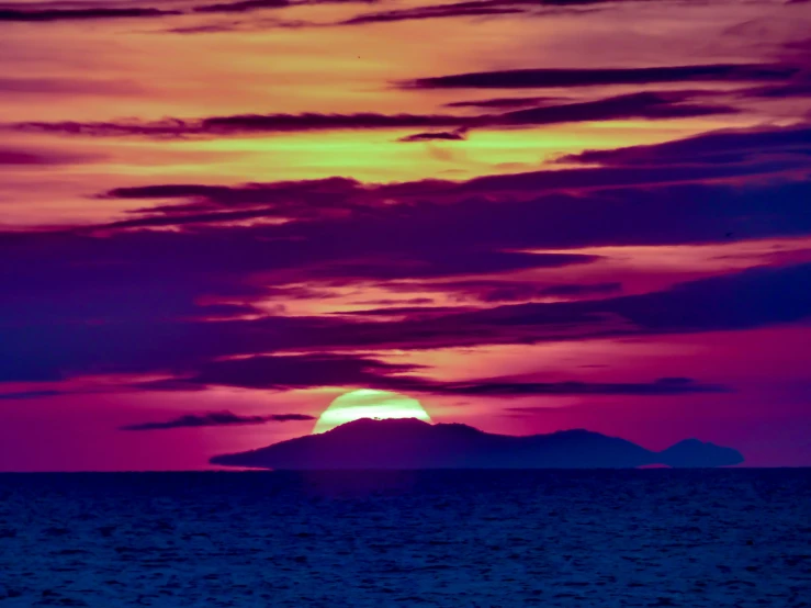 a sunset with a large blue moon and mountains in the distance