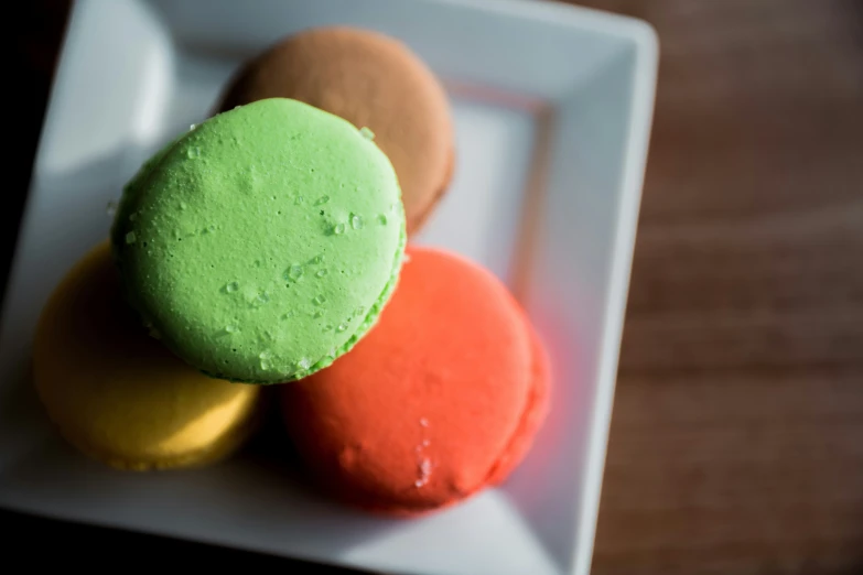 three colorful doughnuts on a white plate on a wood surface