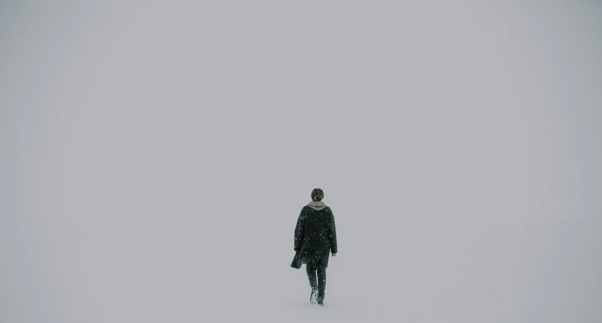 man walking away in the snow alone in the middle of the day