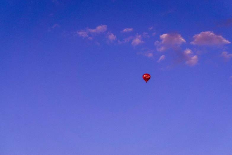 a red balloon flying in the air with a few clouds
