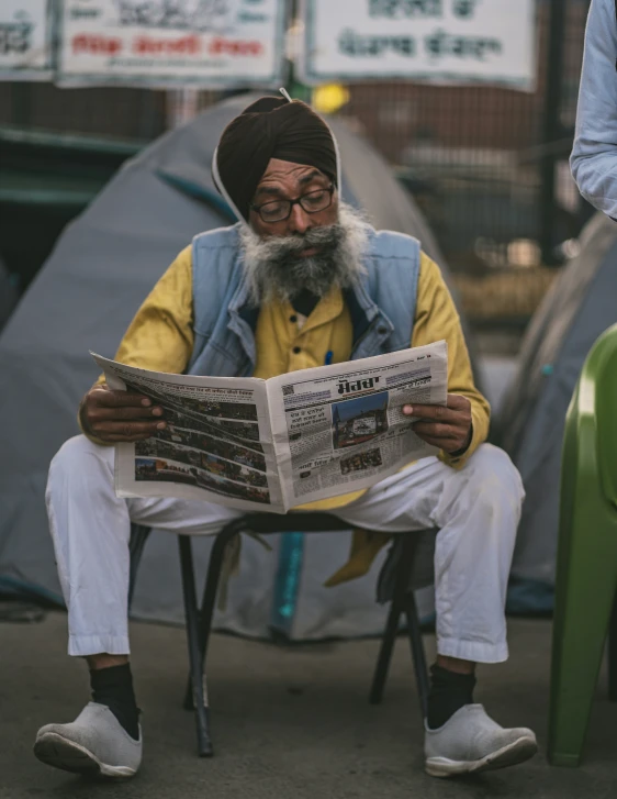 a man wearing a yellow jacket is reading a newspaper