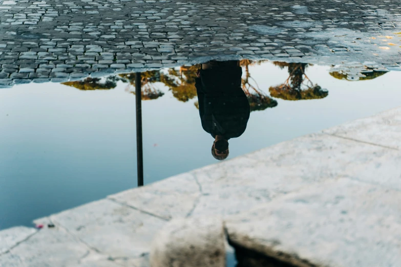 there is a reflection of a person walking and a umbrella and a building