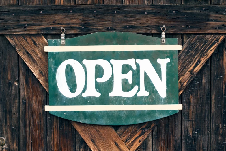 a green sign reading open hangs on a wooden wall