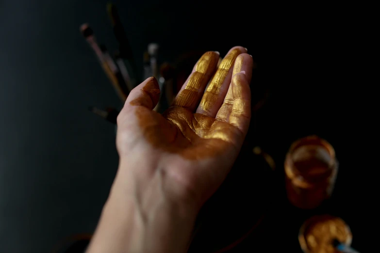 a hand holding out some golden paint next to a bunch of brushes