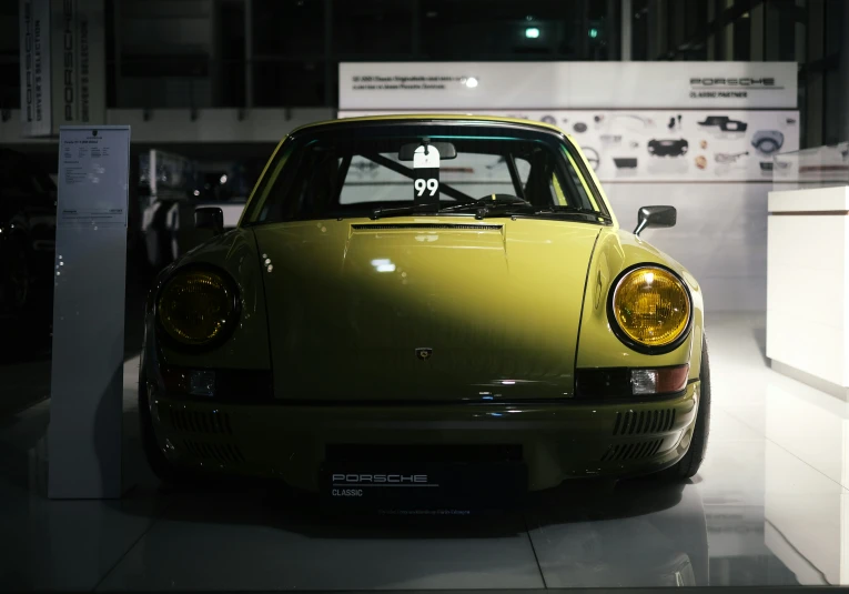 a yellow porsche sits in a display case at night