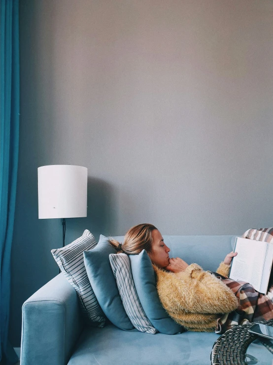 the lady is lying on her couch with her book