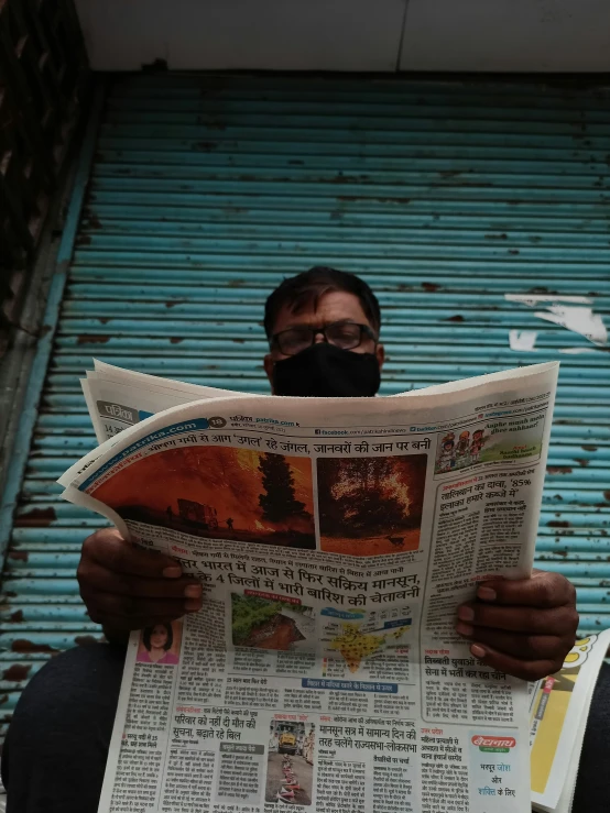 man with mask reads newspaper in front of blue door