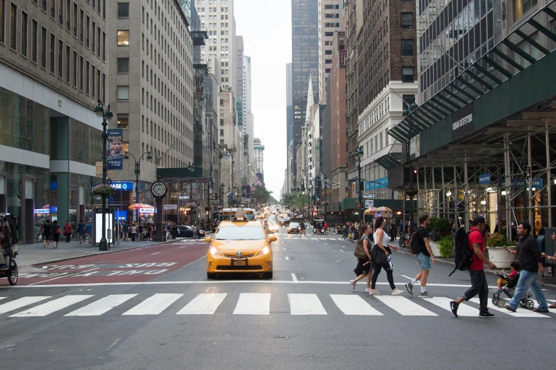 a yellow cab is driving down a street with large buildings