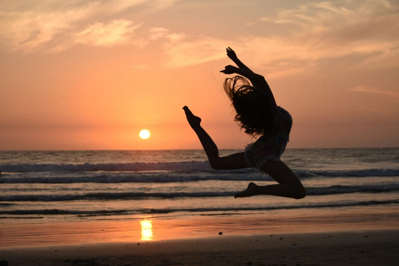 a woman jumping in the air on a beach at sunset
