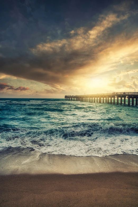 the ocean and pier on the beach at sunset