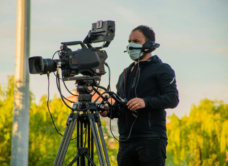 a man wearing a face mask and protective gear stands by an empty tripod looking at camera