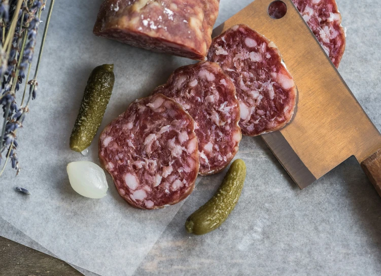 sausages, breadcrumbs, and pickles on top of paper next to a large knife