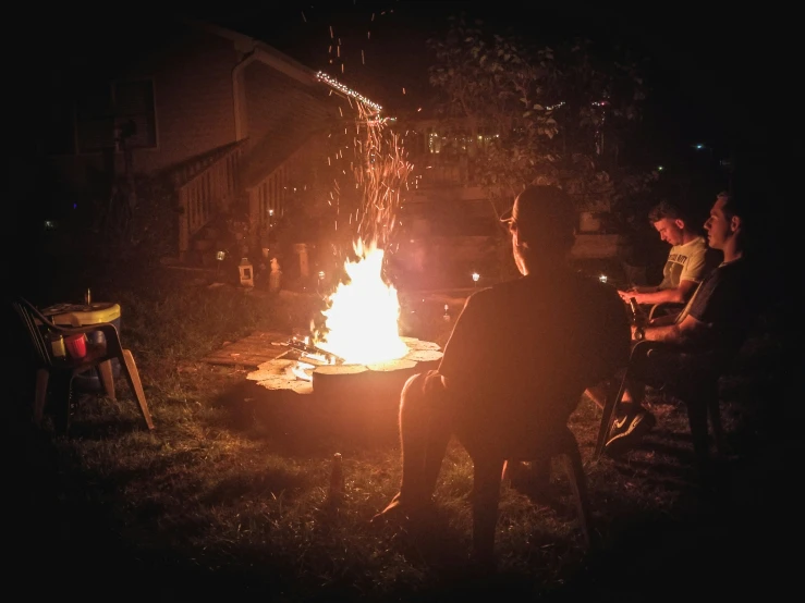 three men sitting at a table with a fire on it