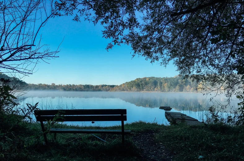 a wooden bench sitting in the foreground near some water