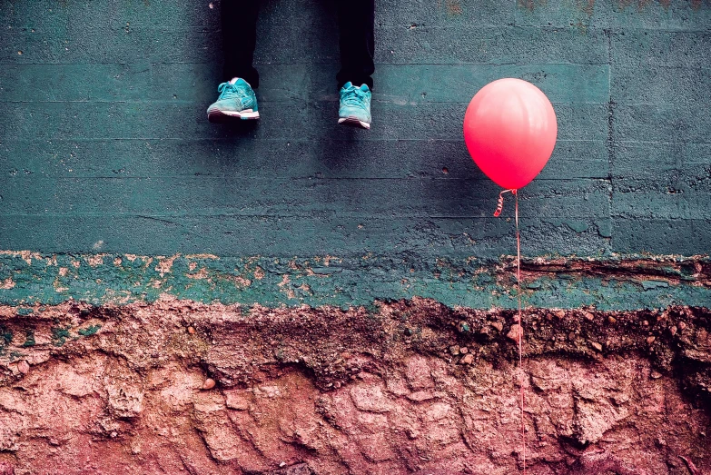 two feet standing on green wall with red balloon and two feet resting on it