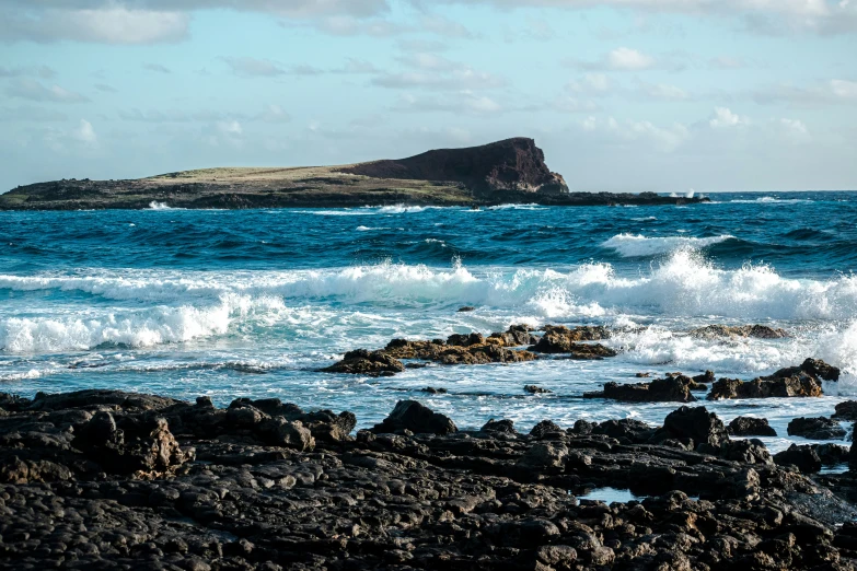 waves crashing on rocks and beach with small island in distance