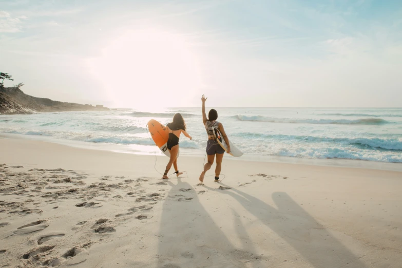 two women carrying surfboards on a beach with waves in the background