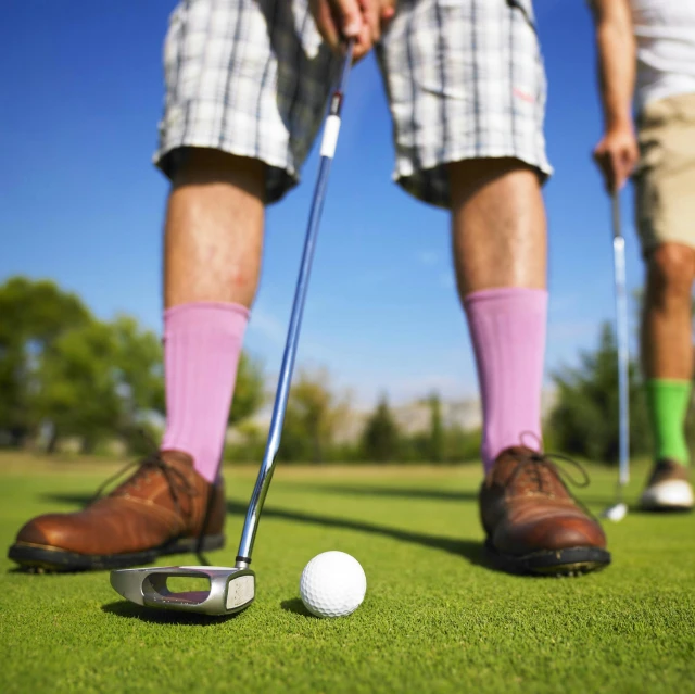 the legs of two people on the grass with a golf ball and driver