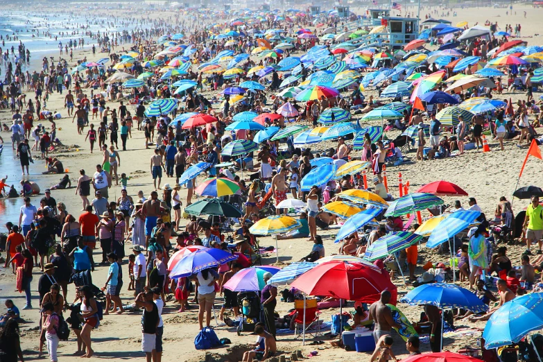 a large number of people at the beach with colorful umbrellas