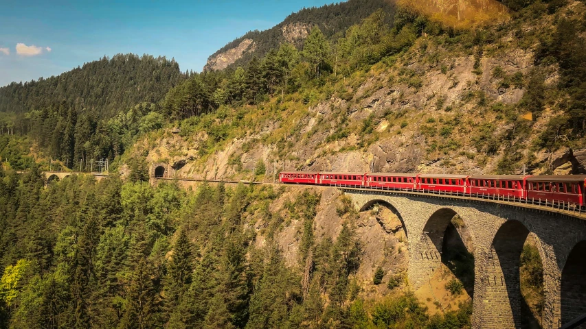 a long train is riding along the train track in the mountains