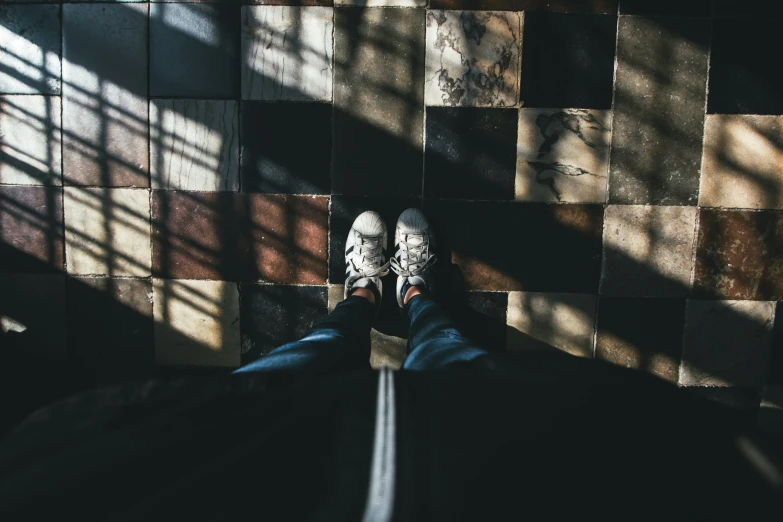 person's feet in white sneakers stand between two brown tiled walls