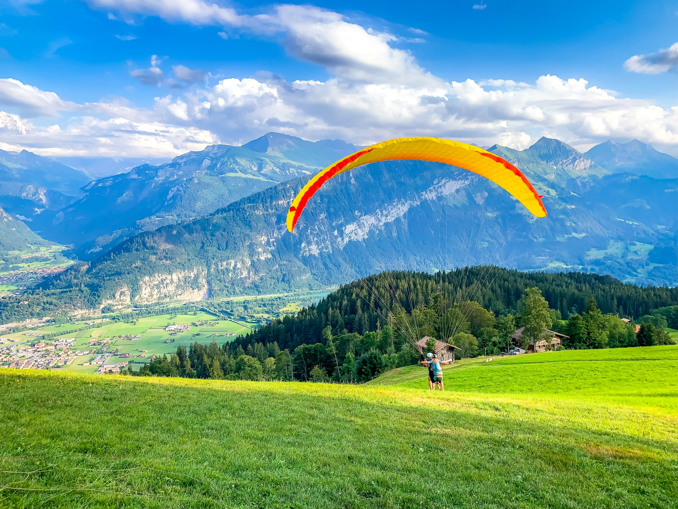 a person flies a yellow para sail over a lush green field