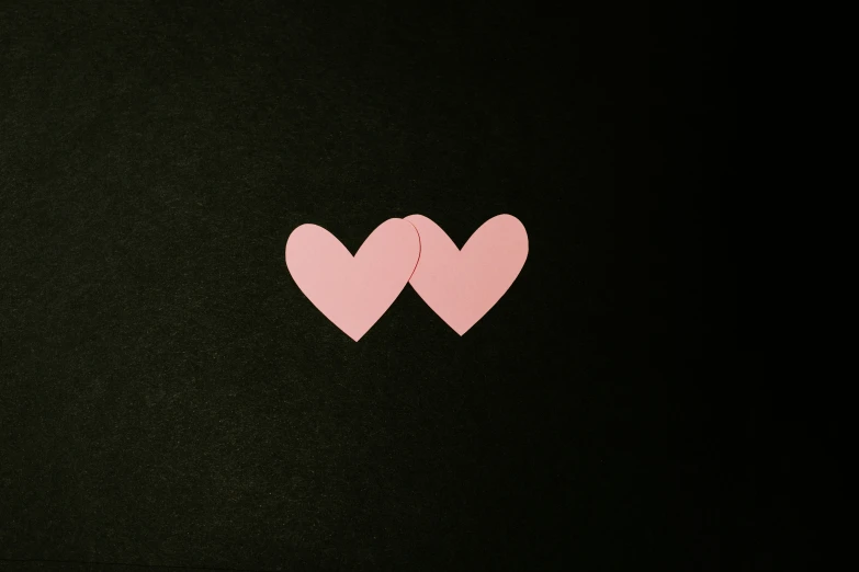 two pink hearts on a black background cut out from small pink pieces