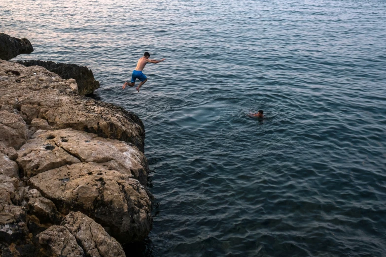 people are swimming off rocks into the ocean