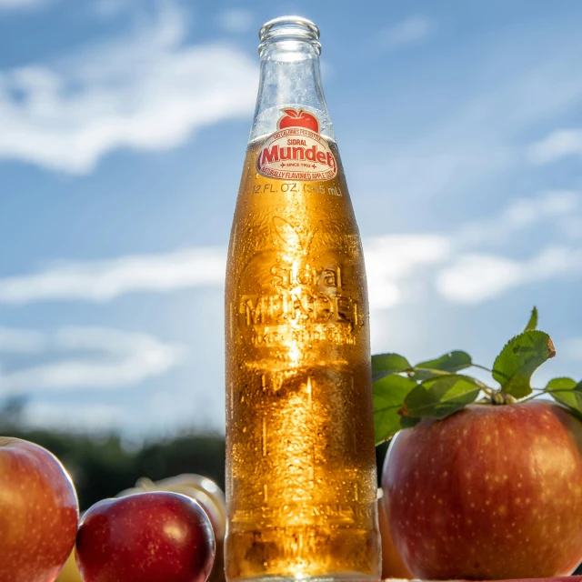 a glass bottle sitting in front of an apple filled box
