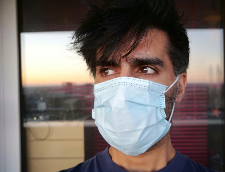 a young man wearing a blue mask, looking out a window