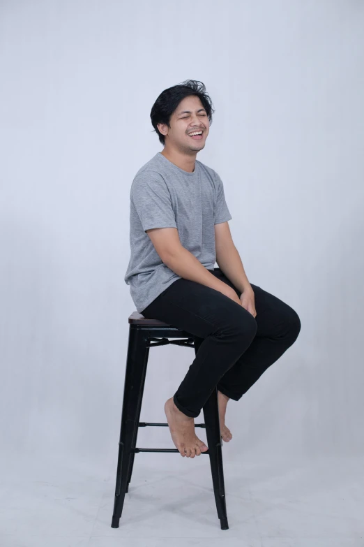 a smiling young man sitting on top of a stool