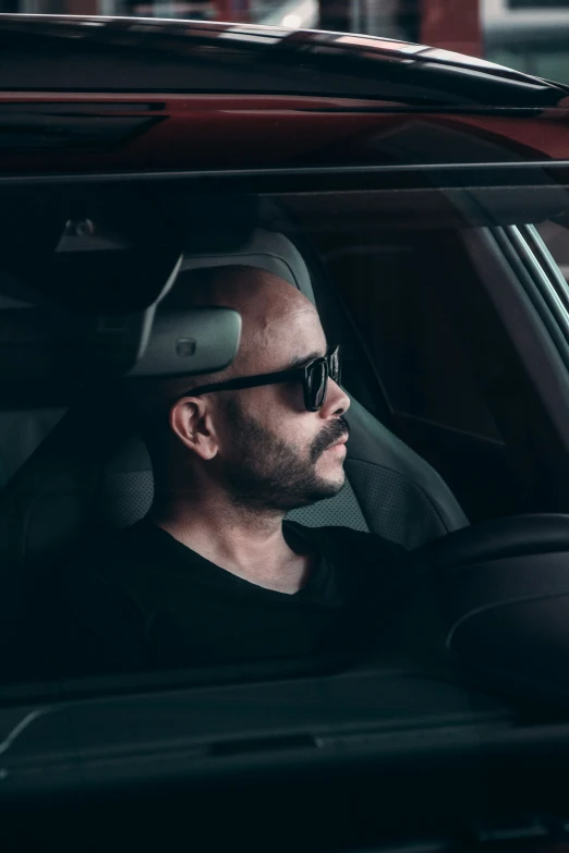 man in sunglasses and cap driving with a black car