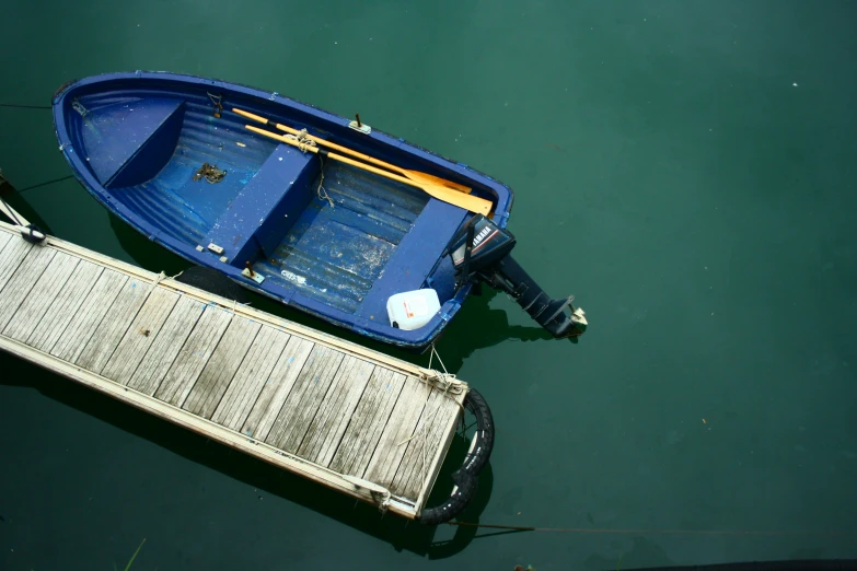 small blue boat floating on green water next to a wooden dock