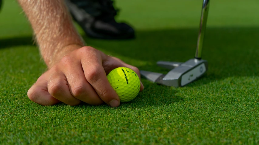 a hand reaches towards a yellow ball laying on top of the green