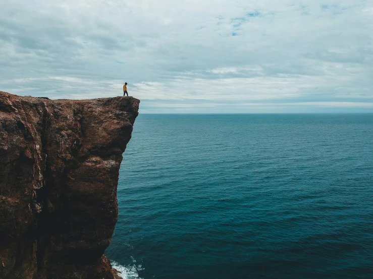 the lone figure is standing on the edge of the cliff